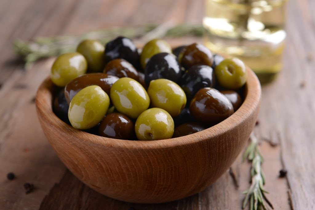 a wood bowl filled with green and black olives.