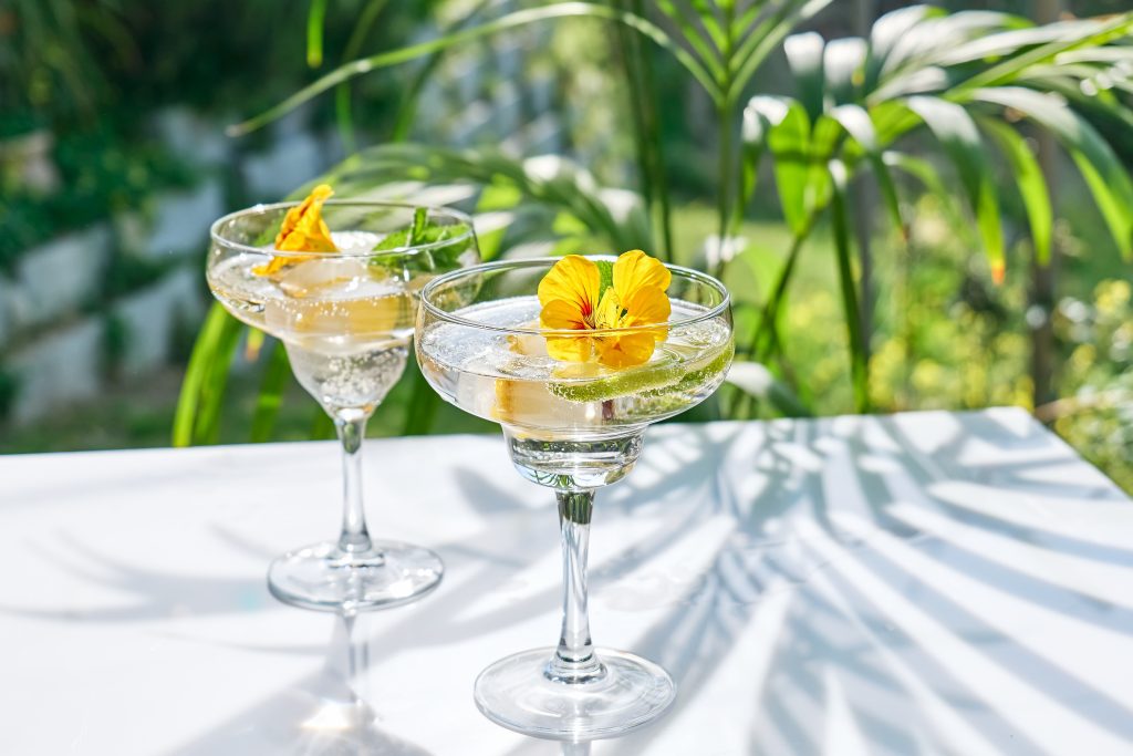 Elegant cocktail with a yellow flower outdoor table, green plant in background.