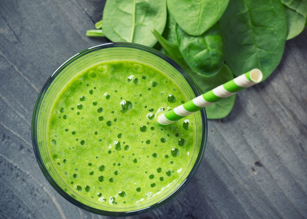 Overhead view of a green smoothie with a striped straw sticking out of it.