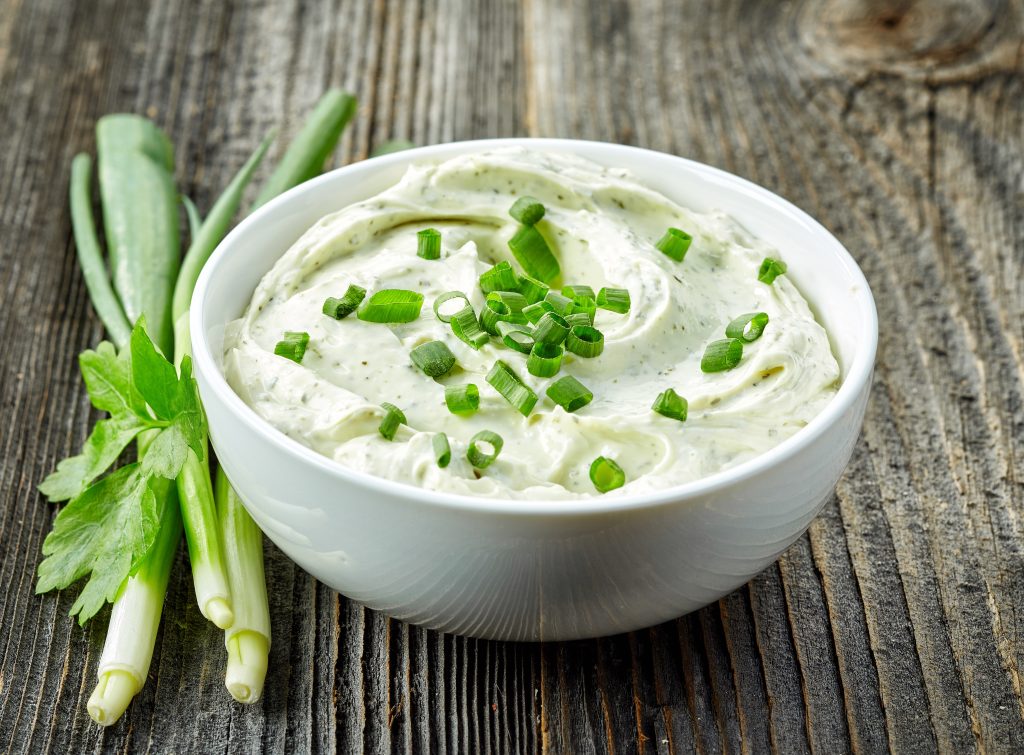 A white bowl with dip in it.  The dip is garnished with green onions and green onions are sitting by the bowl.