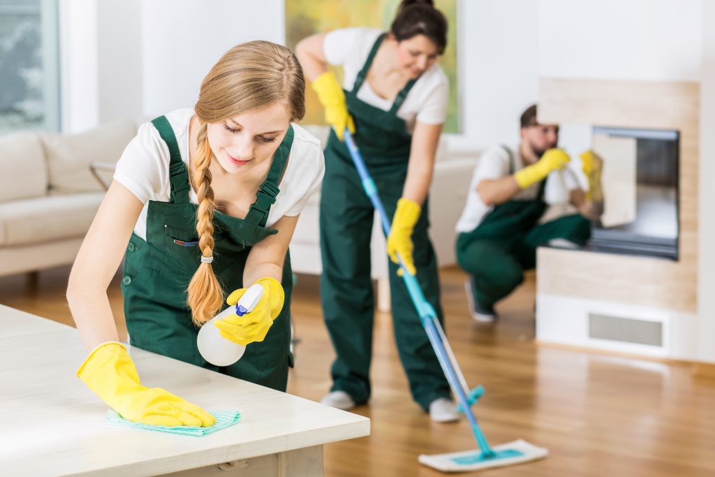 Several people in uniforms and yellow gloves cleaning house.