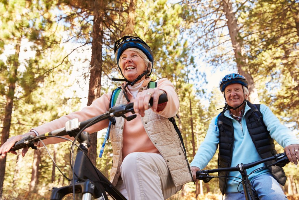 An older man and woman wearing helmets riding bicycles.