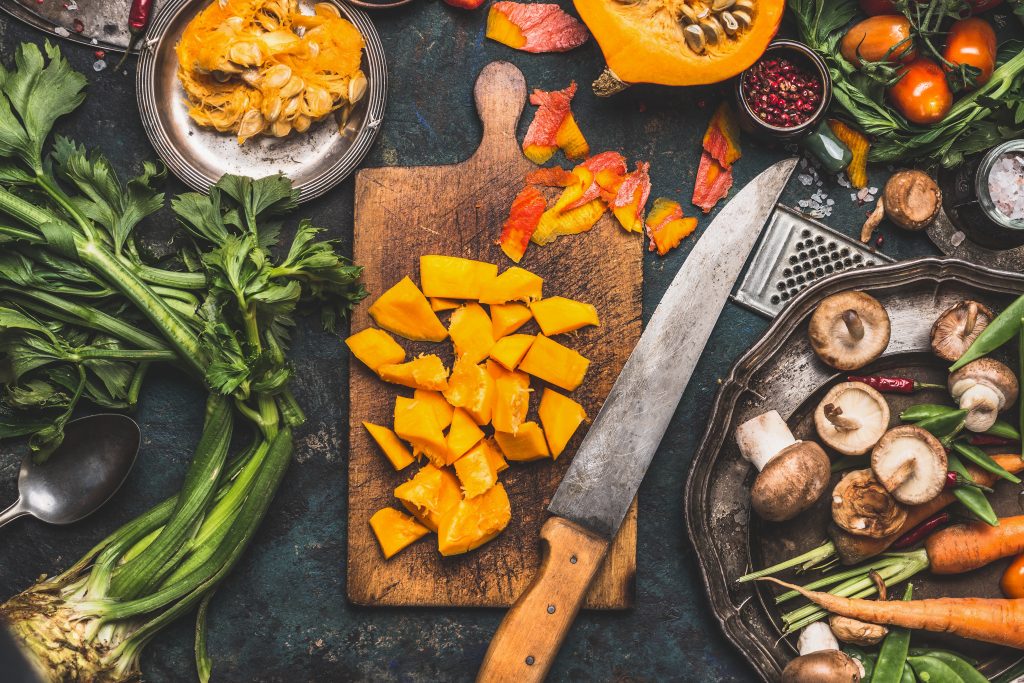 an overhead view of fresh cooking ingredients, a knife a wood board with chunks of butternut squash.