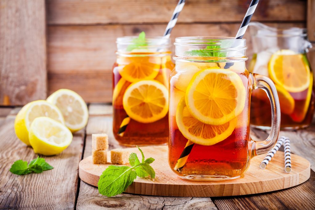 Glasses of iced tea on a wood board. There's striped straws sticking out of them and lemon slices in them.