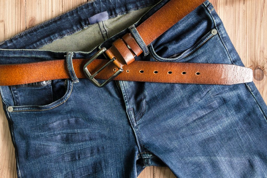 A leather belt looped through a pair of blue jeans.