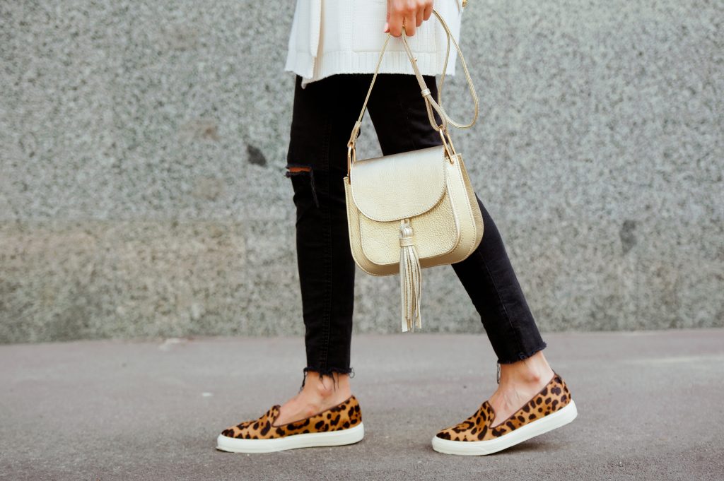 Person walking, wearing leopard sneakers, carrying a white handbag.