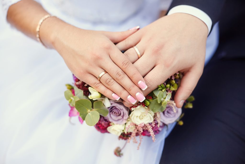 just married husband and wife hands with wedding bands on top of flowers.