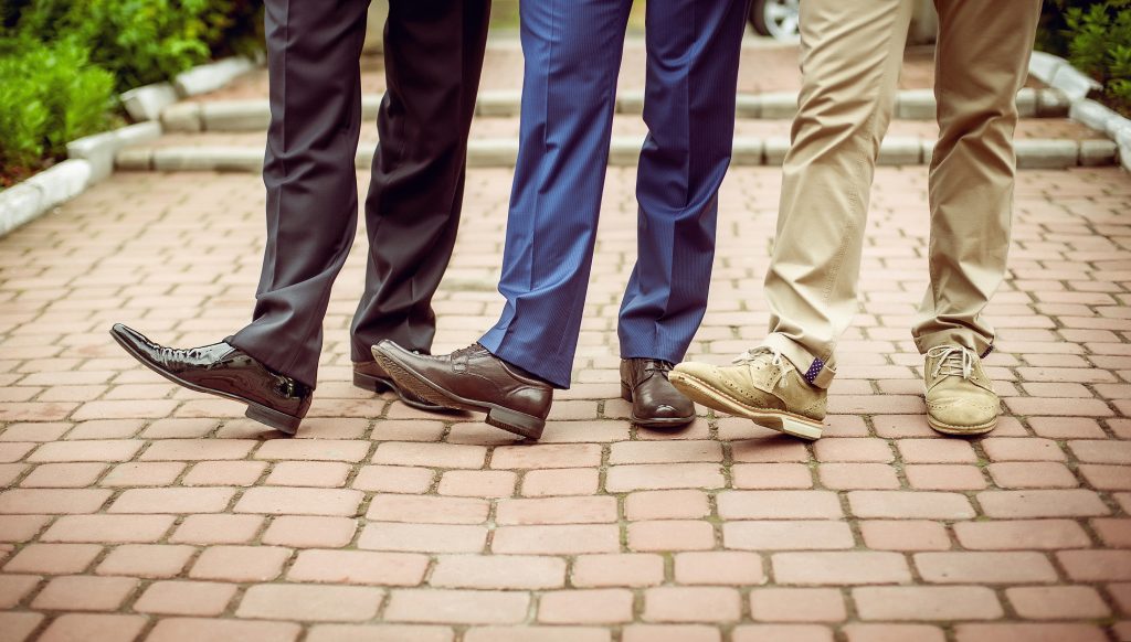 several bottoms of legs of men wearing leather dress shoes. 