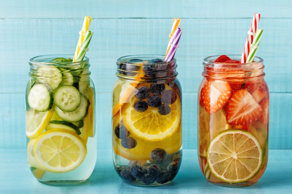 Three clear glasses of Infused water. They all have straws in them and are filled with fruit.