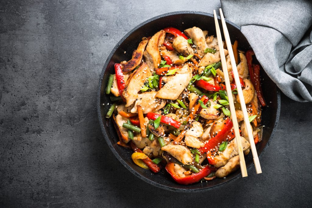 Chicken and peppers stir fry in a black bowl. A pair of chopsticks are laying on top of the bowl.