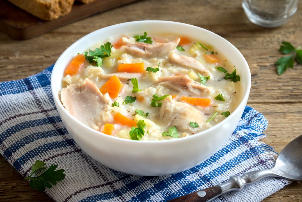 A white bowl with chicken soup in it.  The bowl is sitting on a blue and white plaid towel.