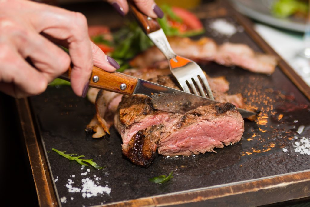 a woman's hands cutting a steak.