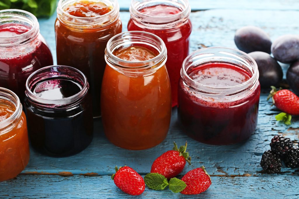 A variety of sizes of jars filled with different flavors of jelly.