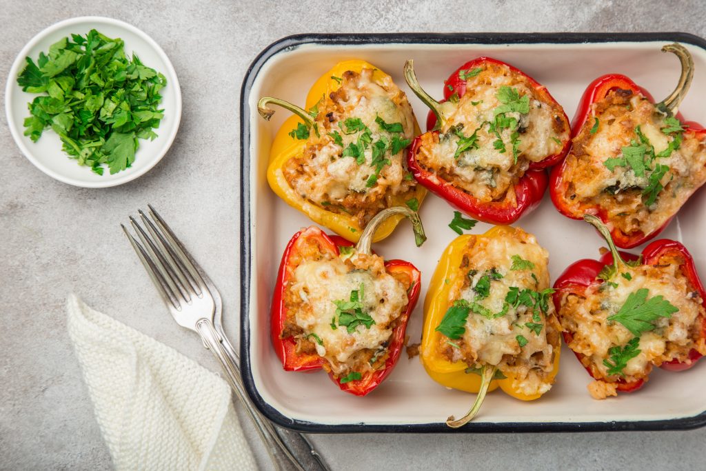 Six Chicken Stuffed bell peppers in a glass dish, they are garnished with parsley. Fresh parsley to the left of the dish.