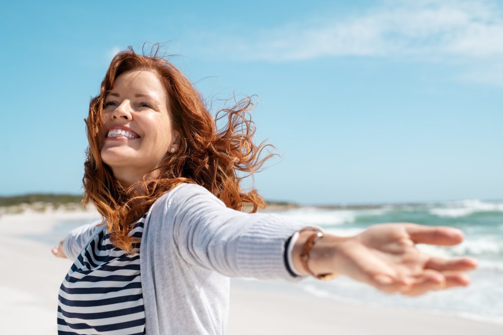 Woman smiling with outstretched arms on a beach.