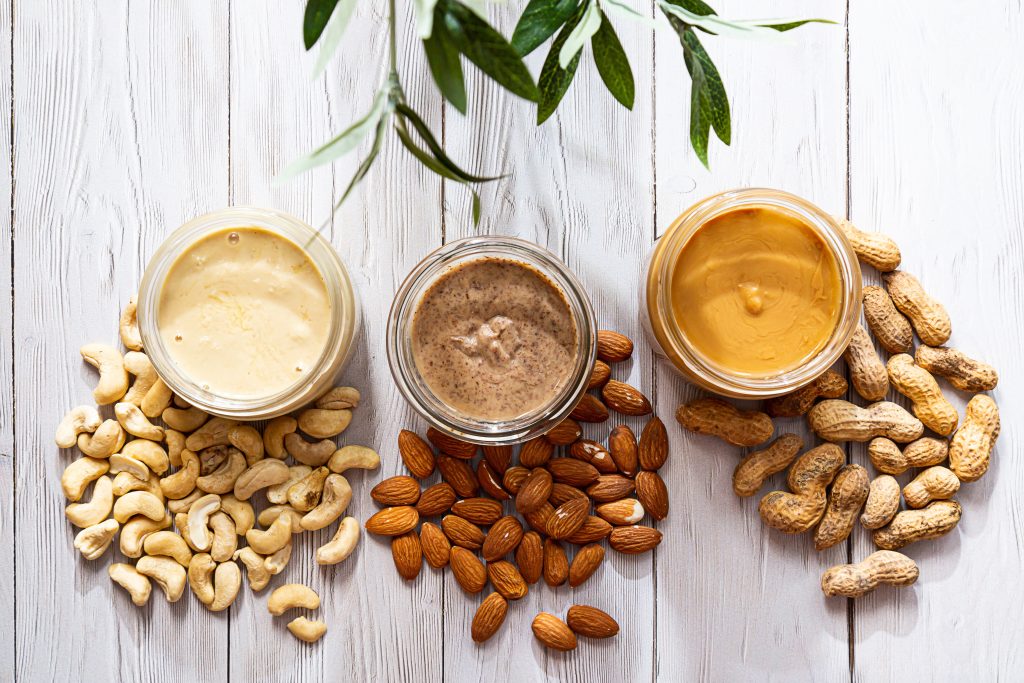 three jars of nut butters, nuts surrounding them.