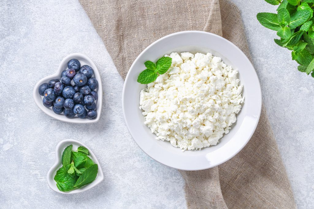 A white bowl of cottage cheese and a white heart shaped bowl of blueberries, mint leaf garnishes.