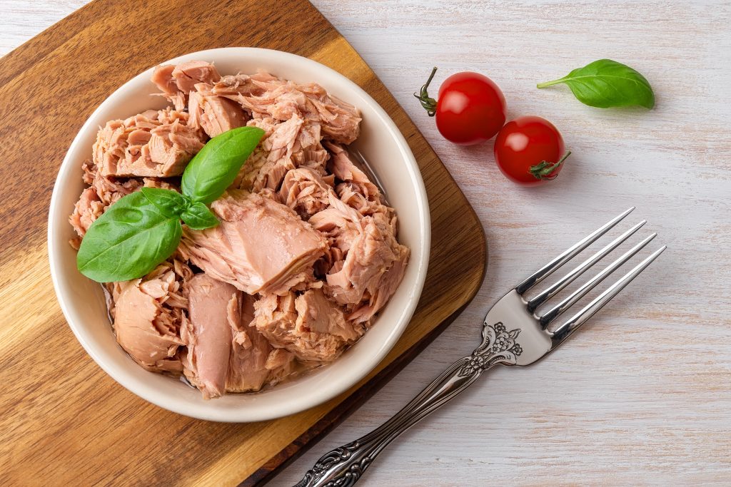 a white bowl of flaked tuna sitting on a wood board, green garnish.