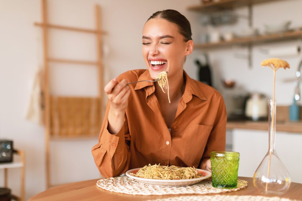 A smiling woman eating pasta.