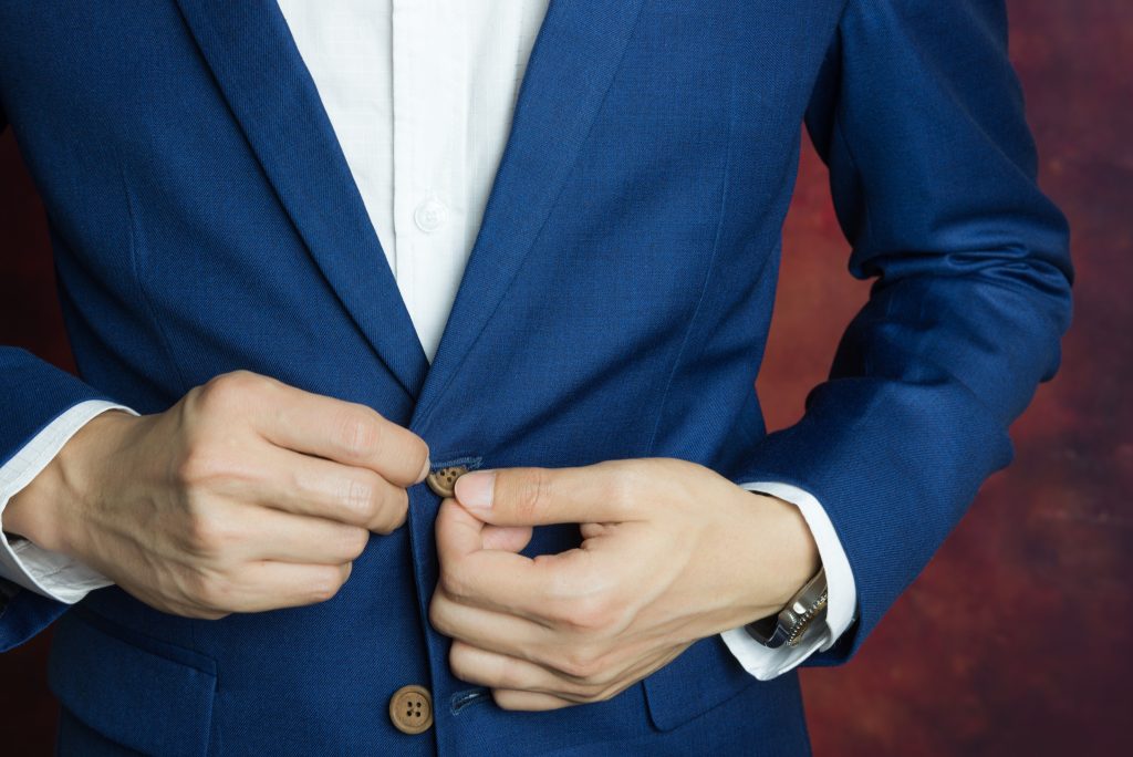 man buttoning jacket on a blue suit.