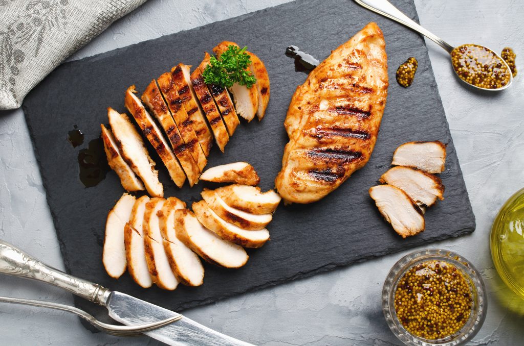 grilled chicken breasts on a black cutting board. one is sliced.