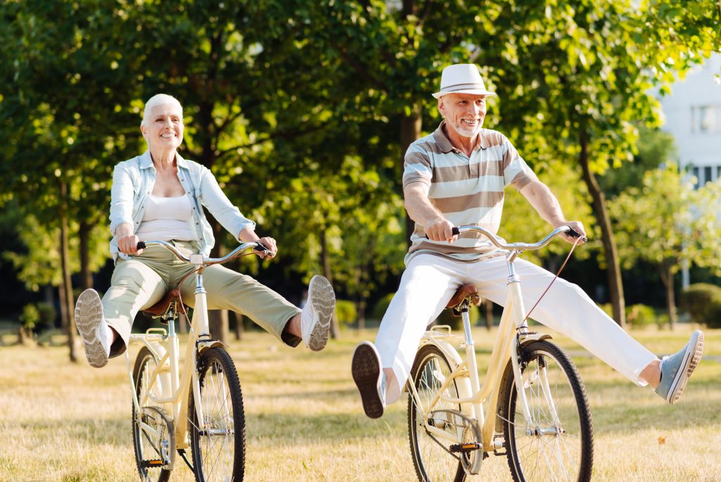 An older man and woman playfully riding bicycles.