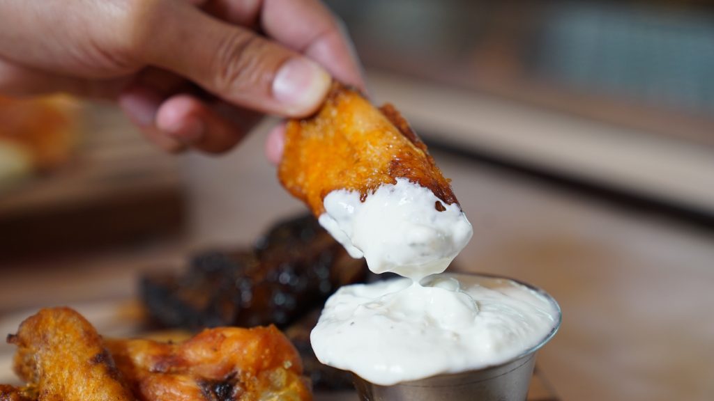 a hand dipping a chicken wing into ranch dressing.