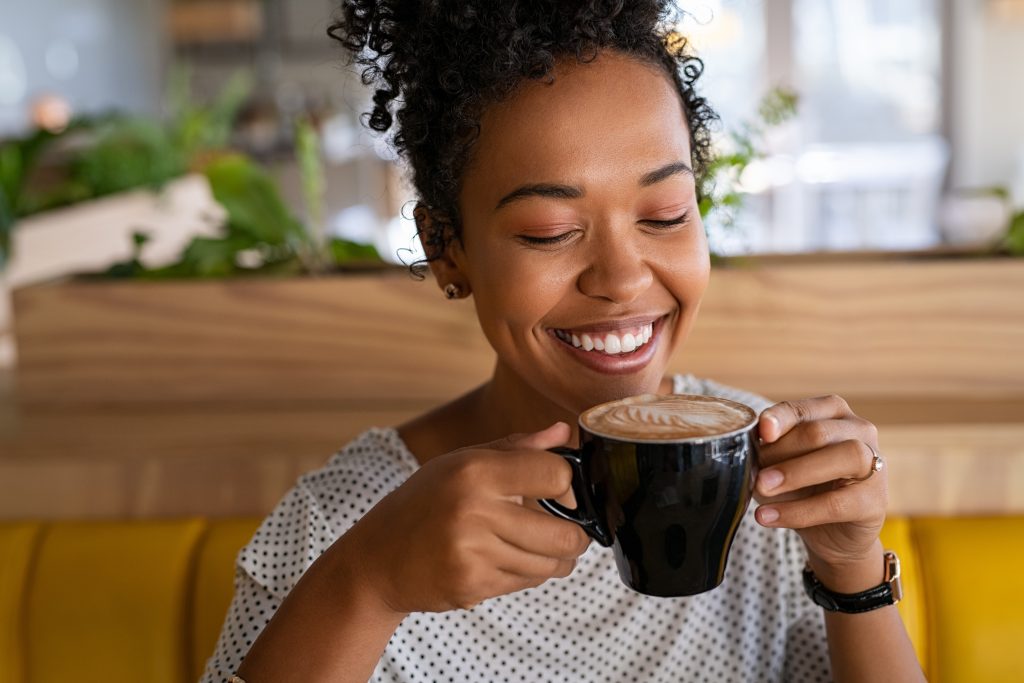 A smiling woman drinking a cup of coffee.