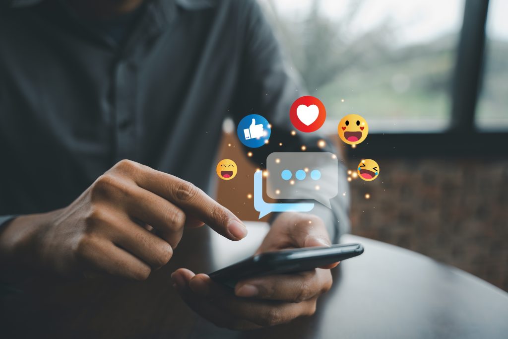social media icon emojis over a hand and a cell phone.