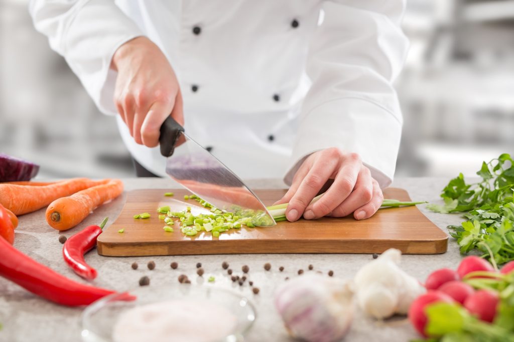 Chef cooking and cutting vegetables with knife.