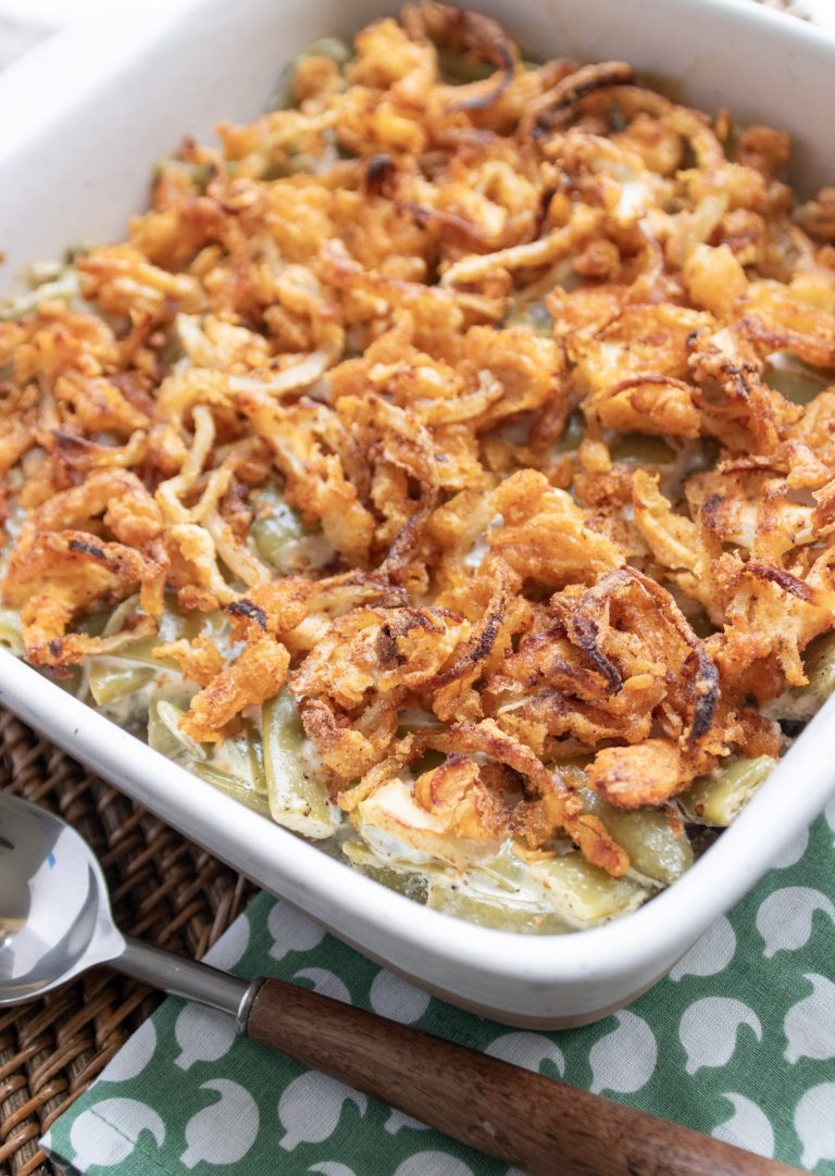 green bean casserole in a white dish. a wood handled spoon beside it. sitting on a green and white napkin.