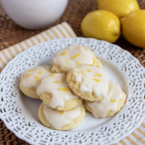 Lemon ricotta cookies on a white plate. 3 lemons to the right of the plate.