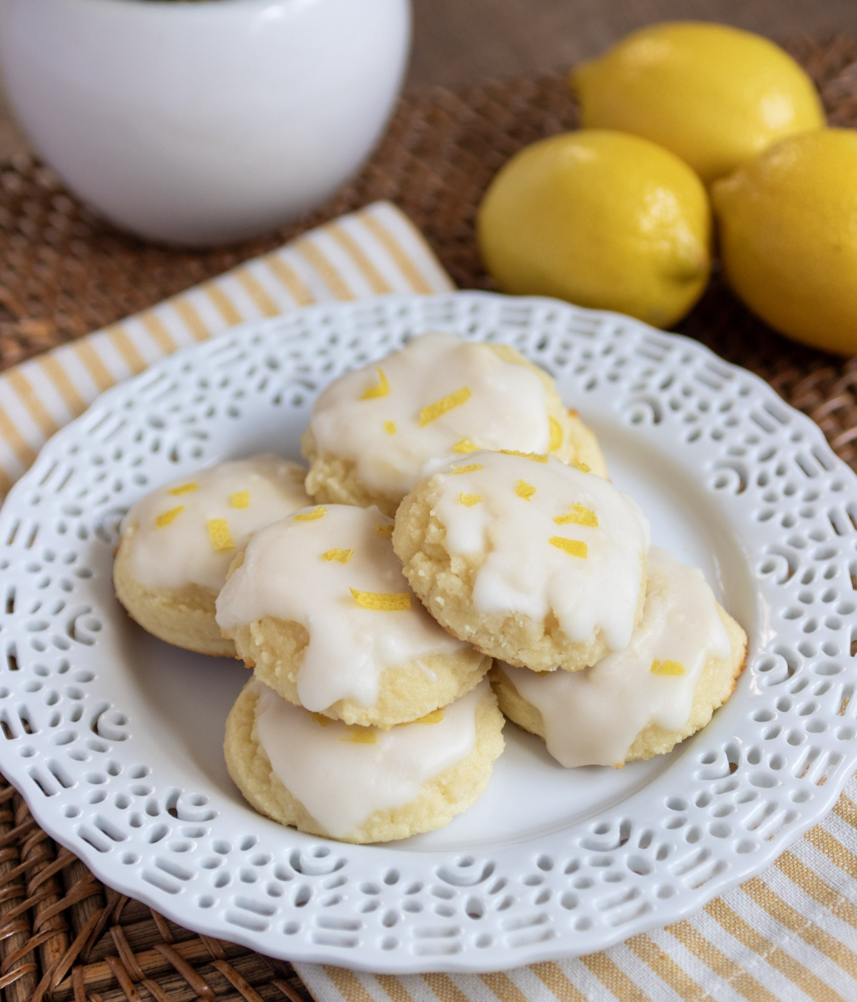Lemon ricotta cookies on a white plate. 3 lemons to the right of the plate.