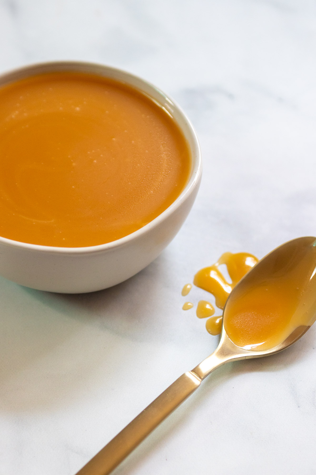 caramel sauce in a white bowl with a gold spoon covered in caramel sauce.