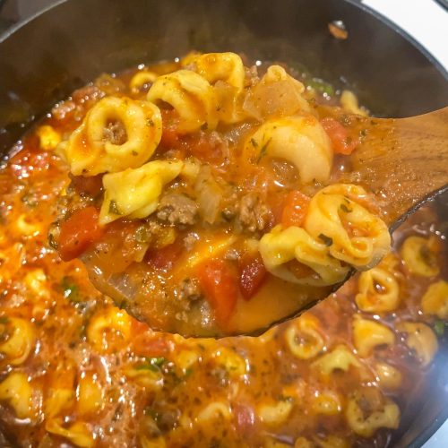 Cheesy tortellini soup on in a pot and on a wooden soup spoon.