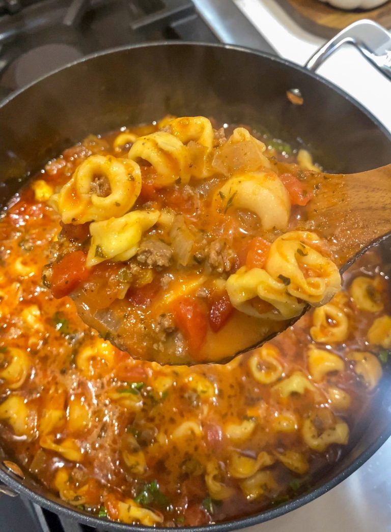 Cheesy tortellini soup on in a pot and on a wooden soup spoon.