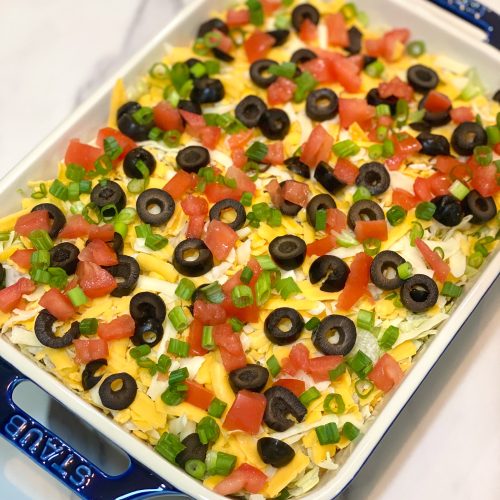 7 layer taco dip in a blue staub glass dish.