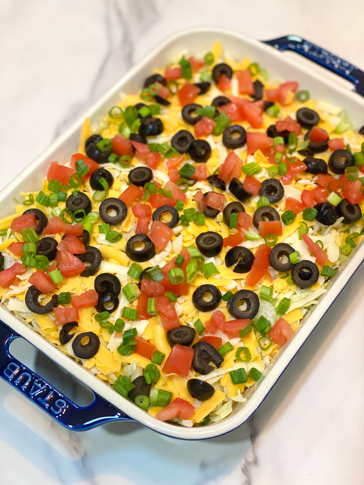 7 layer taco dip in a blue staub glass dish.