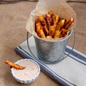 turnip fries in a aluminum bucket with a side of fry dipping sauce in a white dip cup.