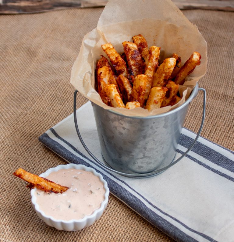 turnip fries in a aluminum bucket with a side of fry dipping sauce in a white dip cup.